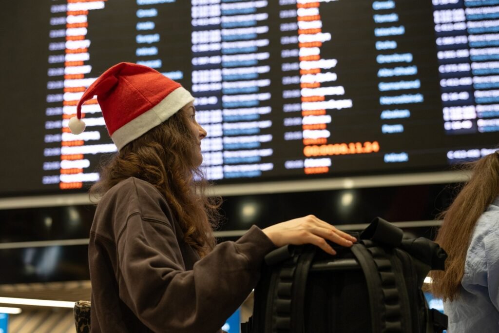 Young woman wearing Santa hat looking at timetable display in airport terminal while waiting for flight departure during Christmas holidays