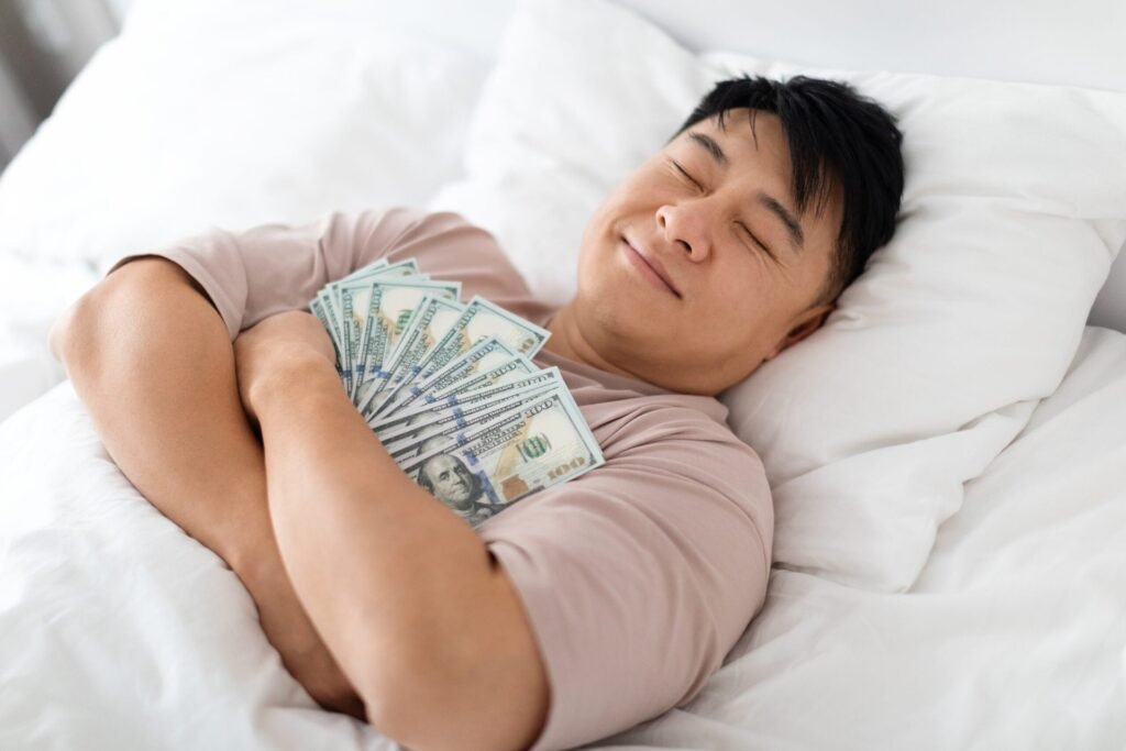 Happy middle-aged man lying in bed with arms full of cash.