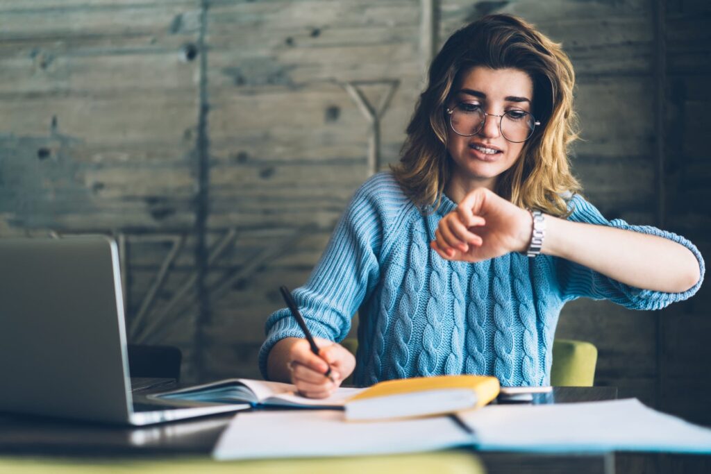 Woman with laptop and notebook looking at her watch