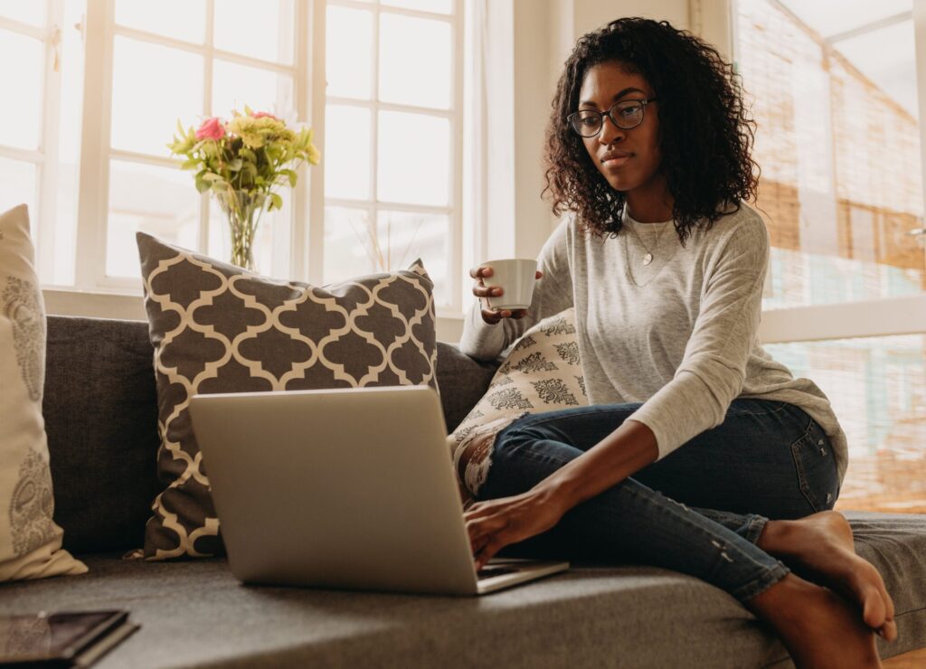 25 of the Best Job Search Sites for Finding Work in 2026 Woman using a laptop on her sofa and drinking coffee