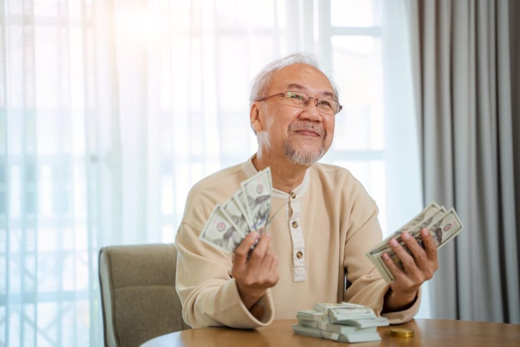 4 Financial Moves to Make in 2026 for a No-Regrets Retirement Senior man smiling and holding wads of cash money for retirement