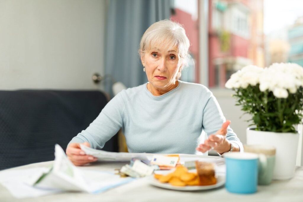 Upset senior woman facing financials troubles, sitting at home table and looking worriedly at papers