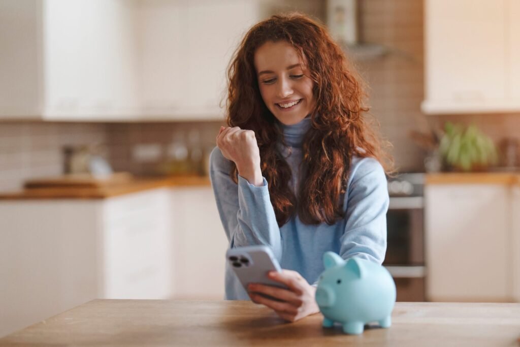 The Best Budgeting Apps for Getting Your Finances Together Excited woman with a piggy bank looking at her phone.
