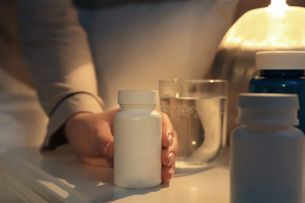 Woman reaching for a bottle of supplement or medication on her nightstand.