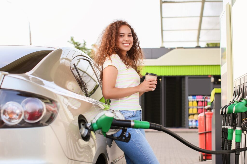 Happy woman pumping gas at the gas station with a fuel discount
