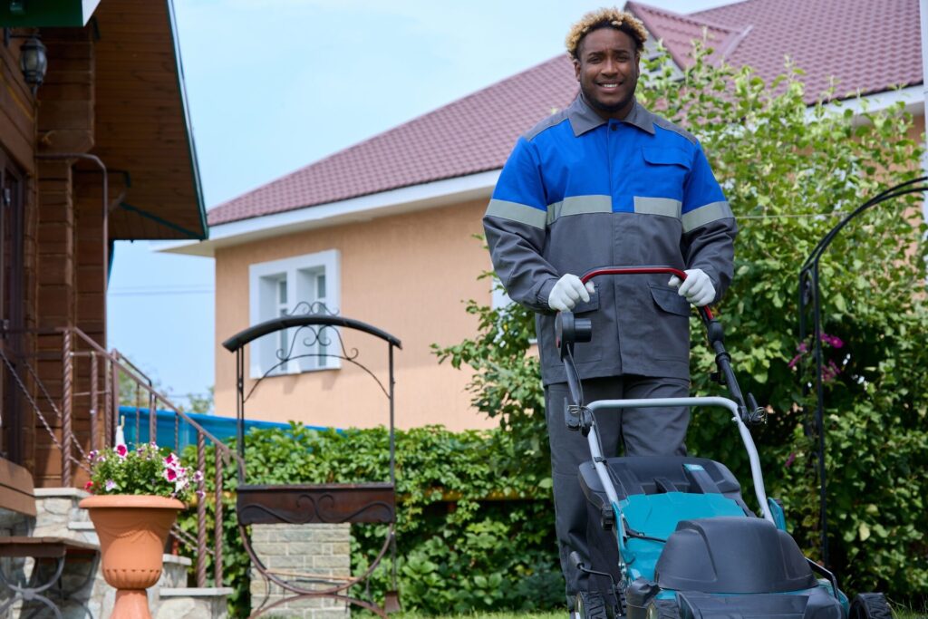 Beat the Pain at the Pump With Everyday Strategies From Lawn Care Experts A man in coveralls uses a lawn mower in a backyard.