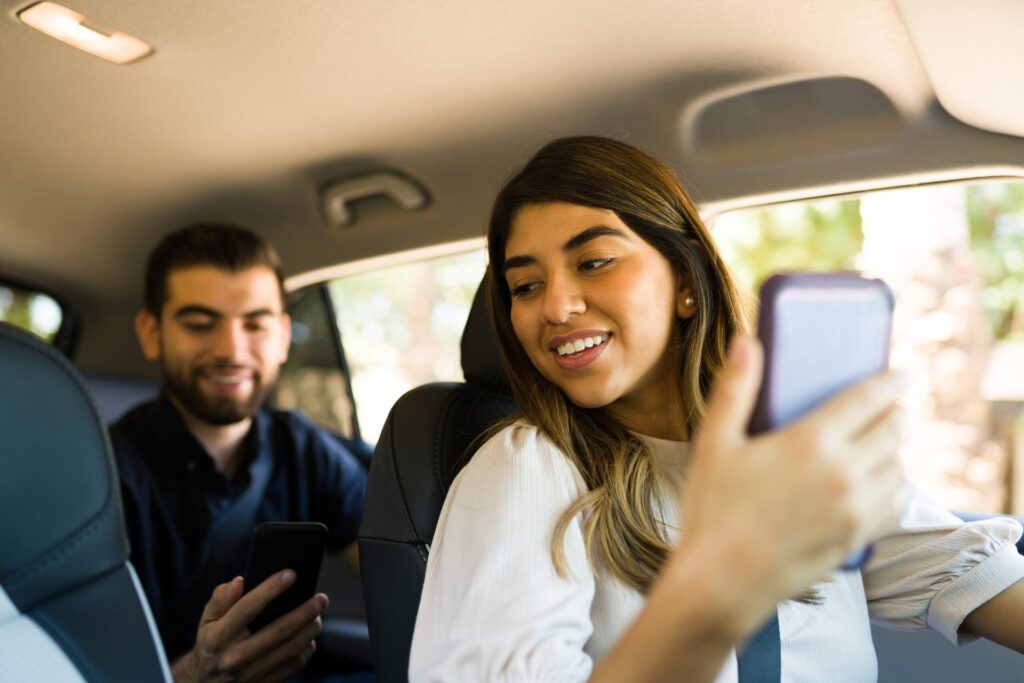 Female driver talking with a man in the back seat while driving. Passenger using a rideshare app